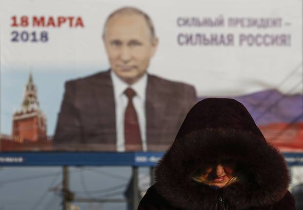 A woman walks past a board, which advertises the campaign of Russian President Vladimir Putin ahead of the upcoming presidential election, in a street in Tula