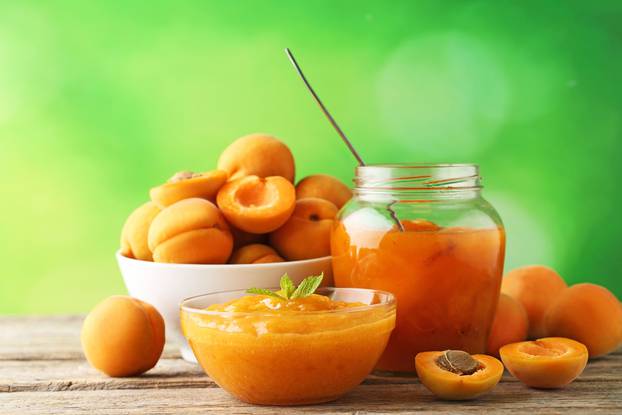 Apricot jam in glass bowl with mint leaf on wooden table