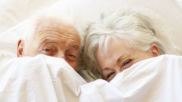 Senior Couple Relaxing In Bed Hiding Under Sheets