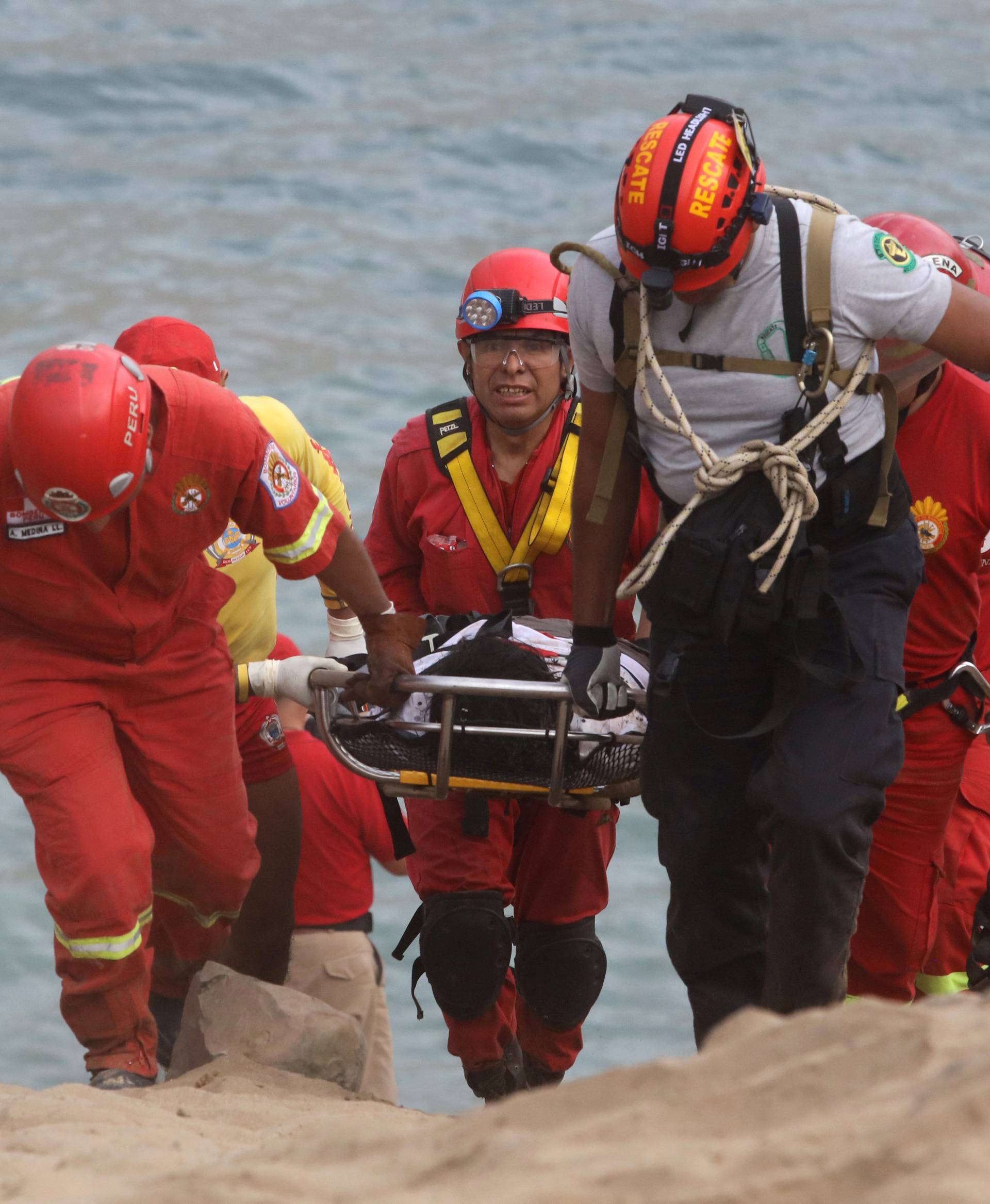 Rescue workers carry victims after a bus crashed with a truck and careened off a cliff along a sharply curving highway north of Lima,