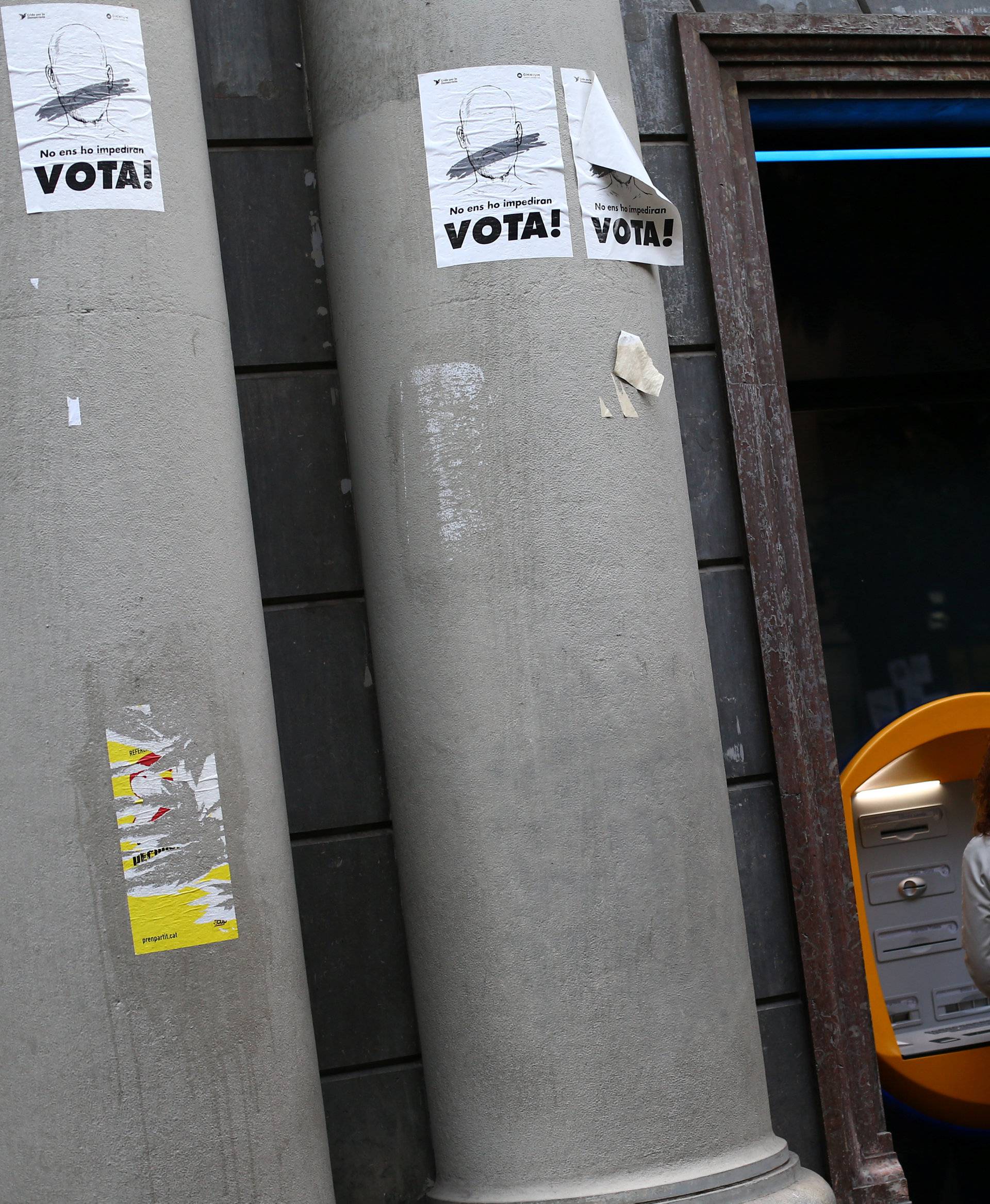 A woman uses a Caixa Bank ATM machine next to signs that read "Vote", on the day of a protest against the transfer of the bank's headquarters out of Barcelona