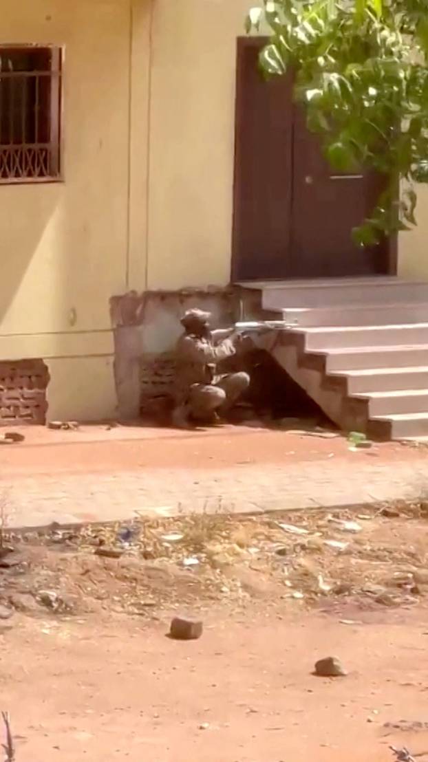 A soldier purported to belong to the Sudanese army crouches down behind a flight of steps, firing a weapon in Khartoum