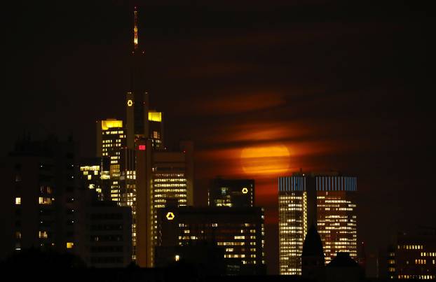 The moon is partly covered by clouds as it rises above the skyline of Frankfurt 