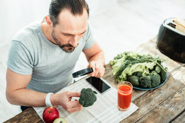 Interested attentive man sitting and overlooking a broccoli.