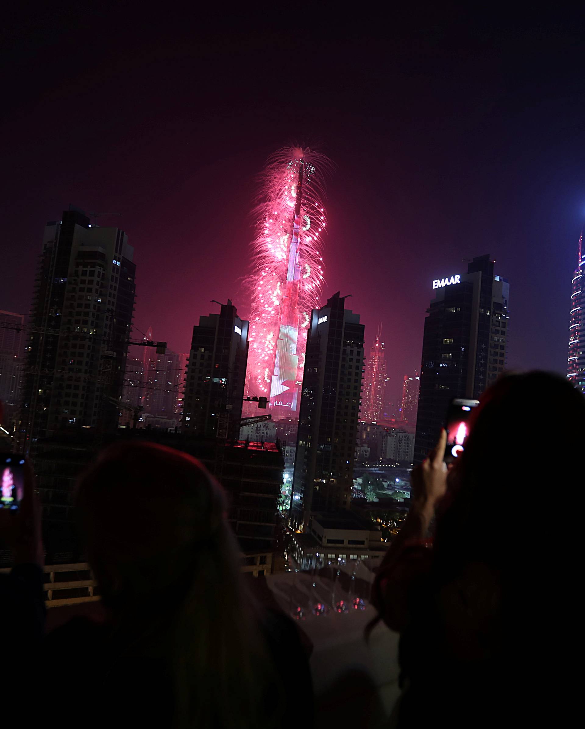 People use their phones to take photos of the Burj Khalifa as it is lit up during New Year celebrations in Dubai