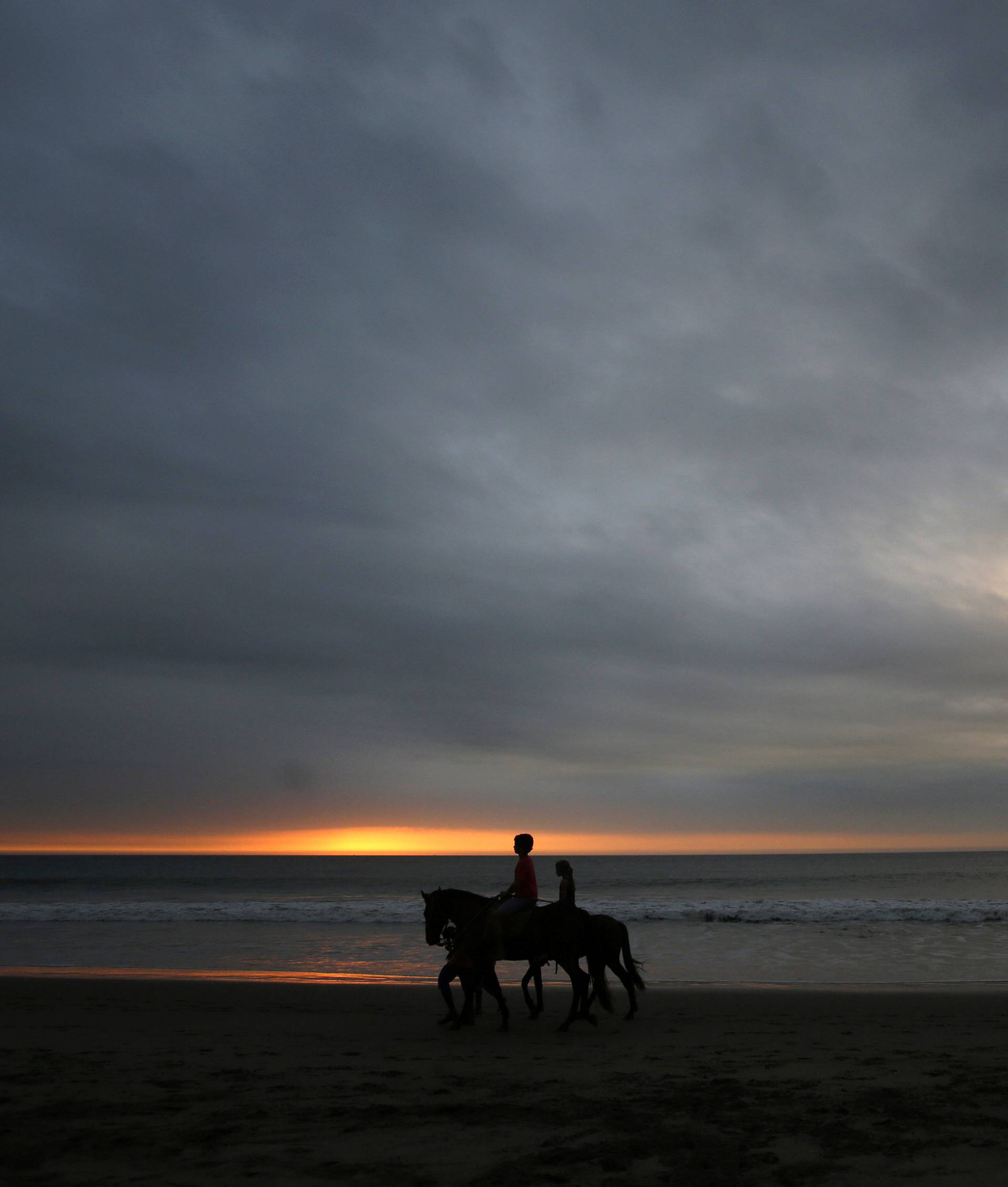 People riding horses by shoreline of the tourist beach of Mancora in Piura