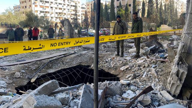 Police officers stand on the rubble of a damaged building at the site of a rocket attack, in central Damascus' Kafr Sousa neighborhood