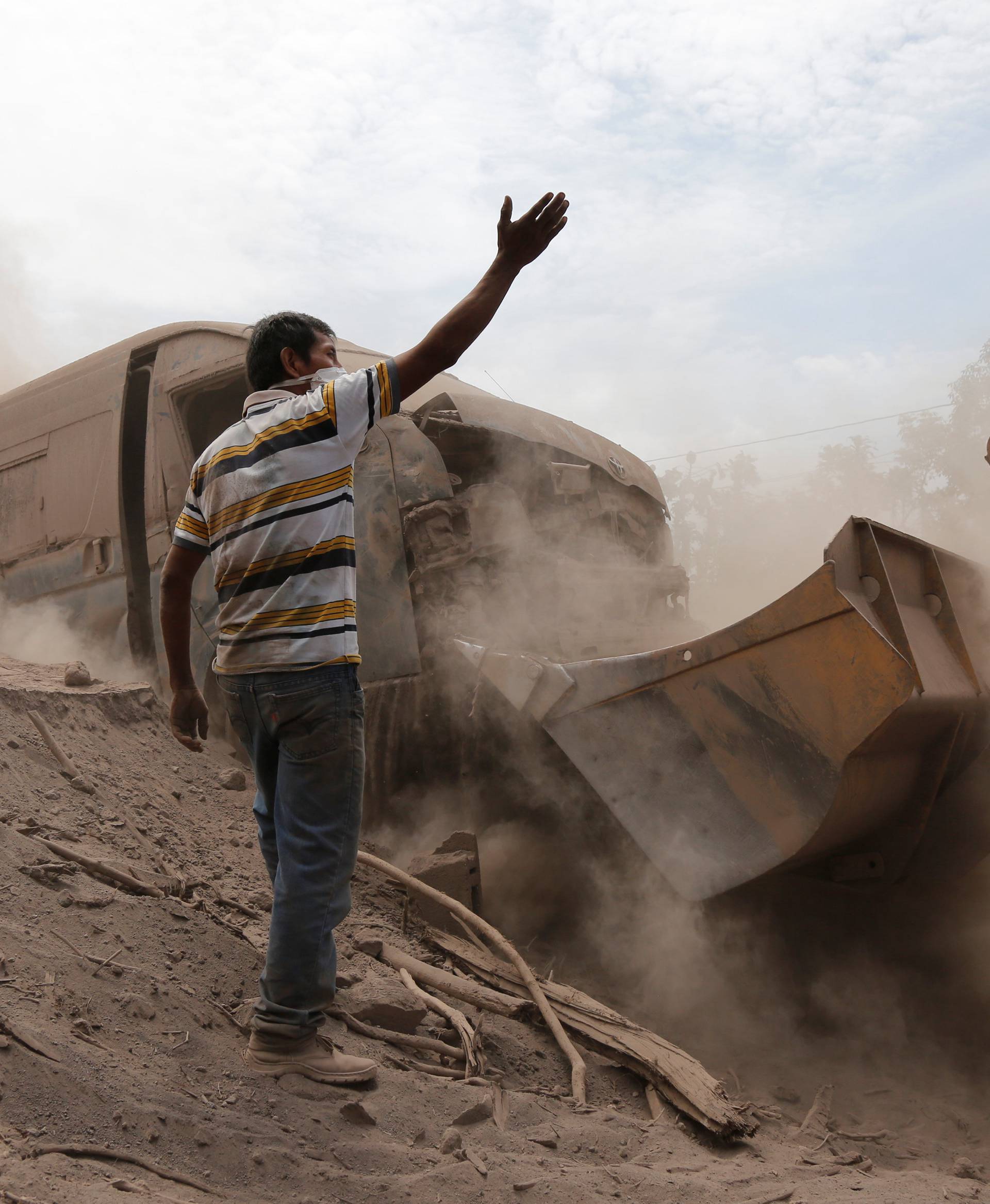 A man gestures as a power shovel removes ash at an area affected by the eruption of the Fuego volcano in the community of San Miguel Los Lotes in Escuintla