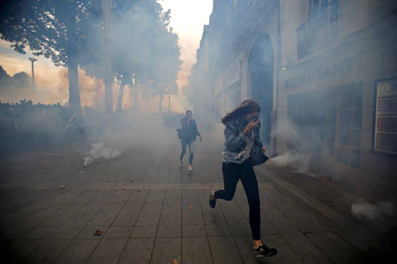 People run away from tear gas during clashes with French riot police at a march in Nantes