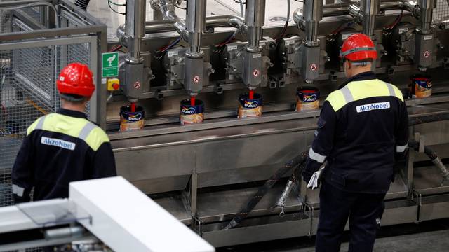 Workers look on as Dulux paint cans are filled on the production line inside AkzoNobel's new paint factory in Ashington, Britain