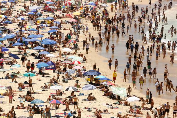 Beachgoers sit and walk in the water at Sydney