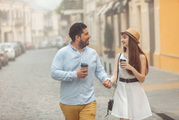 International couple in love drinking coffee walking around the city, holding hand