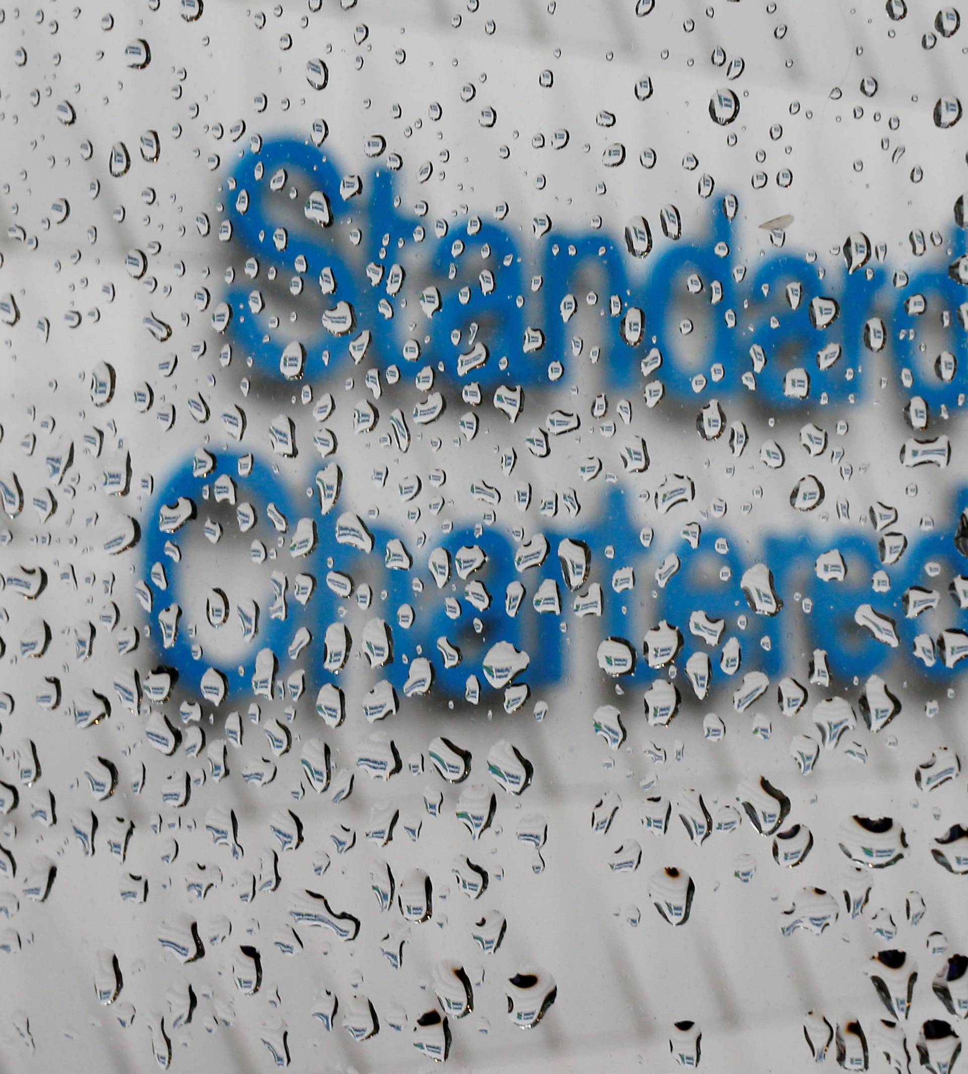 A Standard Chartered logo at its headquarters is seen through a window with raindrops, in Hong Kong