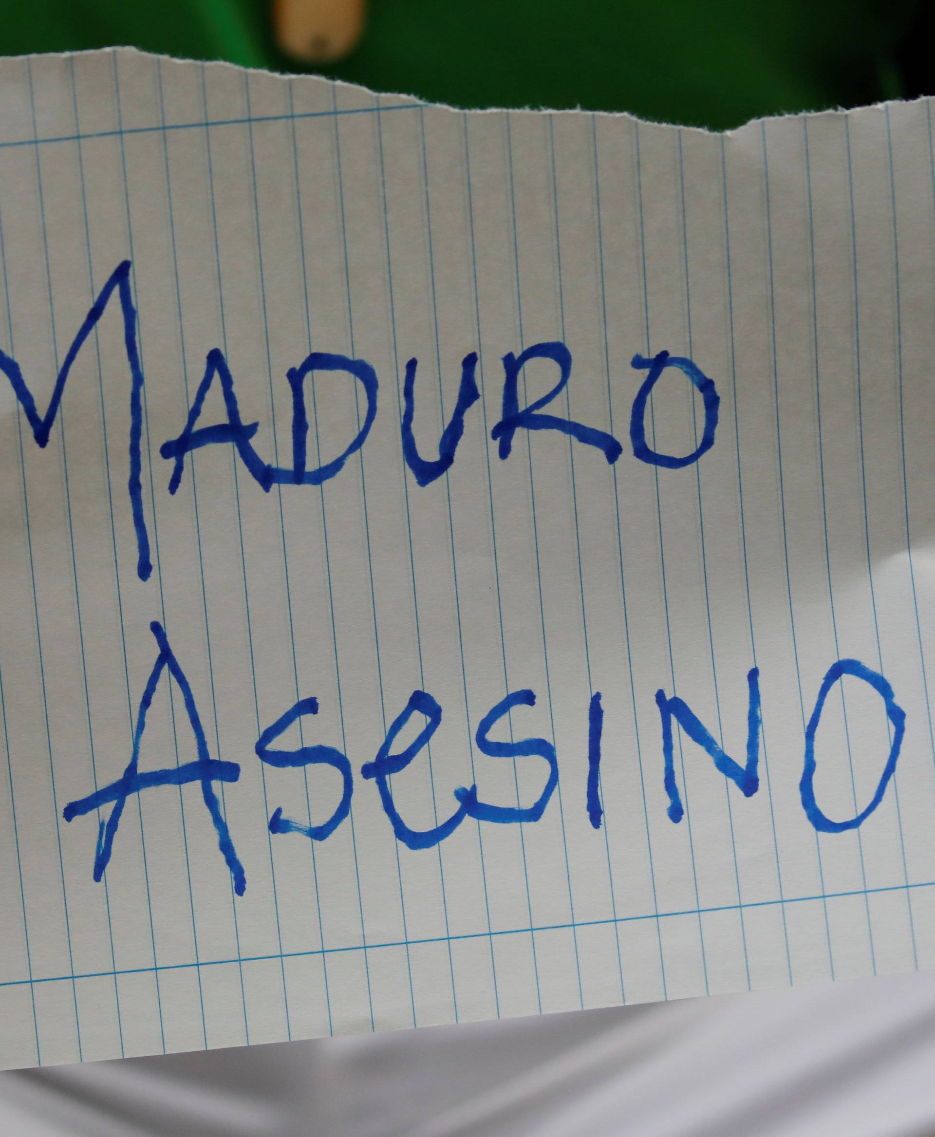 A mourner of the municipal lawmaker Fernando Alban holds a placard that reads, "Maduro murderer", during a gathering outside the headquarters of Bolivarian National Intelligence Service (SEBIN) in Caracas