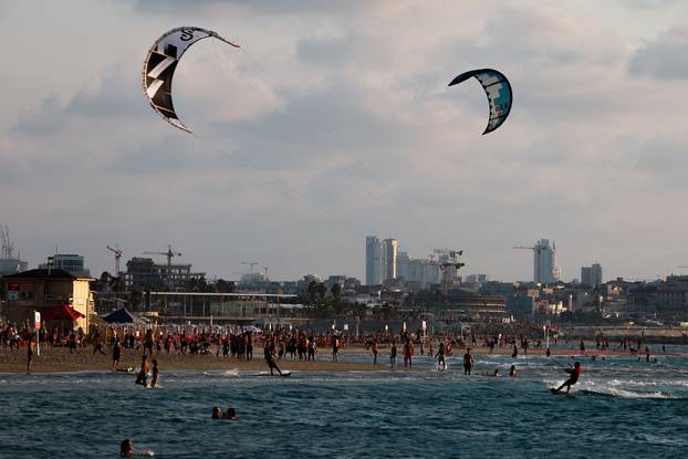 People enjoy the beach as kite-surfers catch the wind in the Mediterranean sea amid the ongoing conflict in Gaza between Israel and Hamas, in Tel Aviv,