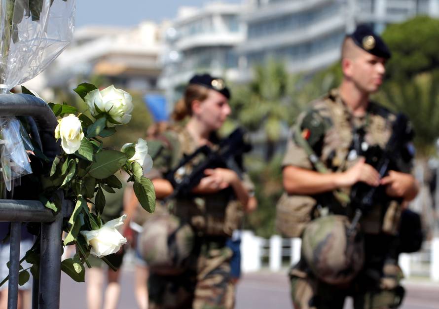 Armed French soldiers patrol near a bouquet of white roses left as part of the commemorations of last year's July 14 fatal truck attack on the Promenade des Anglais in Nice