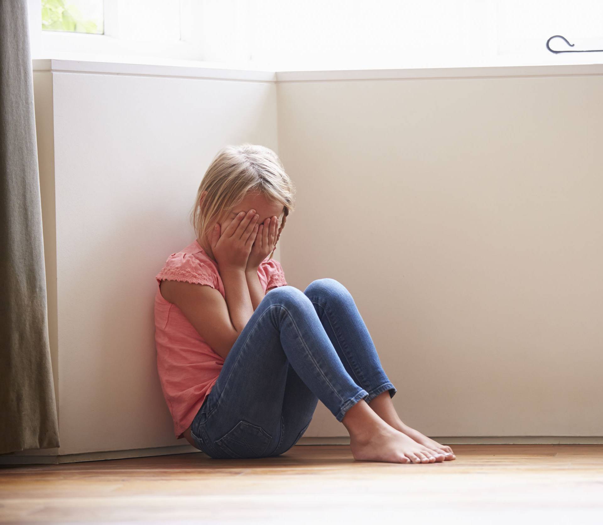 Unhappy Child Sitting On Floor In Corner At Home