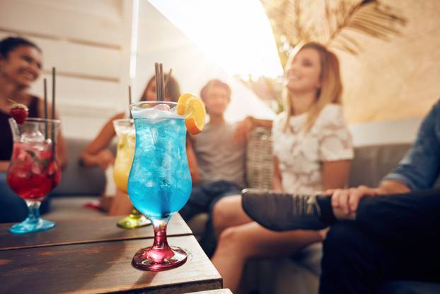 Cocktails on table with young people partying on rooftop