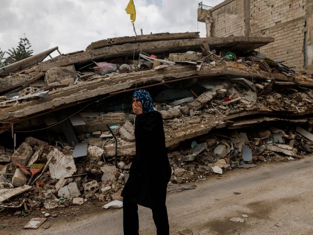 A resident walks while covering her nose to protect against the smell rising from a building containing homes and a restaurant hit by an Israeli strike hours before the ceasefire in Zrarieh