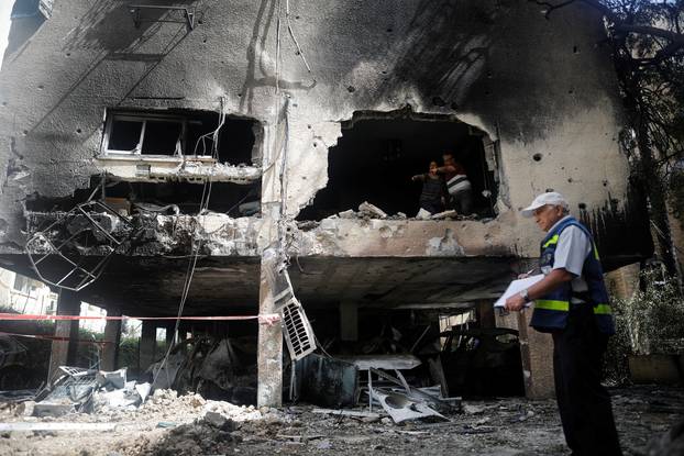 People stand at the scene and survey the damage after a rocket launched overnight from the Gaza Strip hit a residential building in Petah Tikva