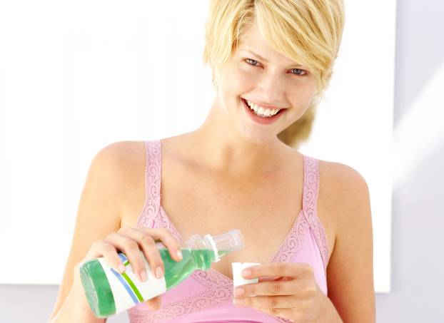 portrait of a woman taking mouthwash in a cup