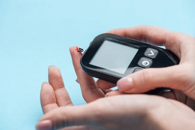 cropped view of female hands testing glucose level with glucometer on blue background