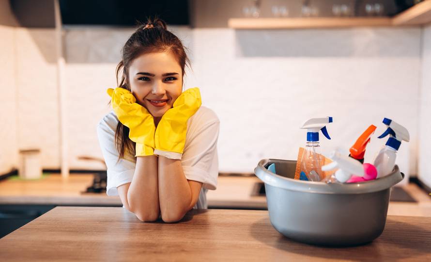 Pretty woman in protective yellow gloves is smiling in the kitchen while cleaning.