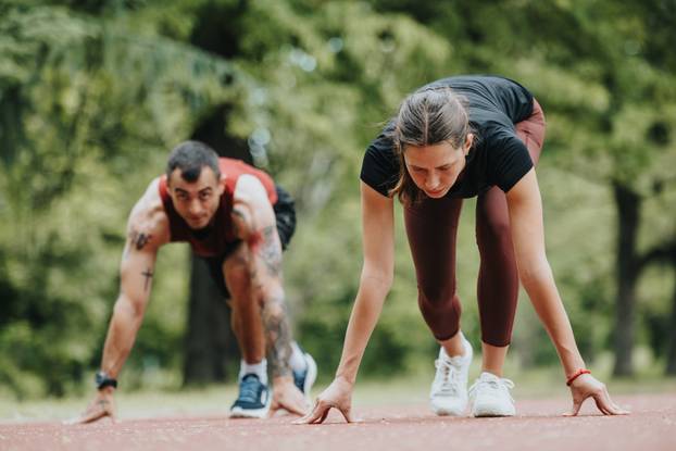 Sports enthusiasts preparing for a sprint on a park track, surrounded by nature