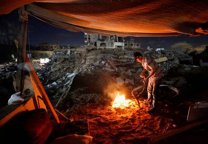 A Palestinian man lights a fire amid the rubble of his house which was destroyed by Israeli air strikes during the Israel-Hamas fighting in Gaza
