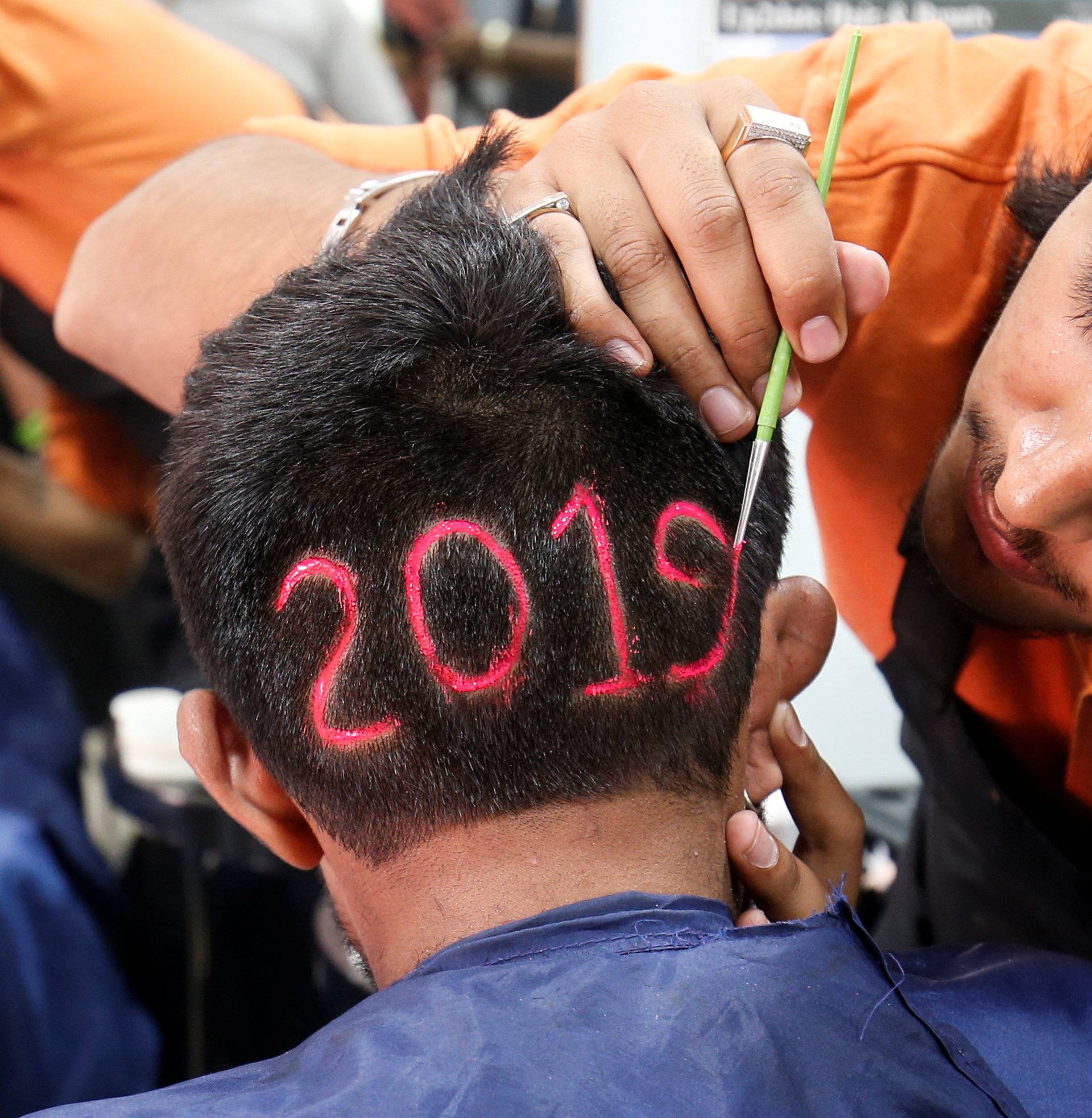 A man applies colour to a haircut with the number "2019", depicted to welcome the new year at a barbershop in Ahmedabad