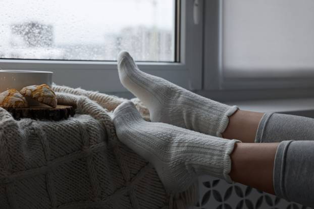 Woman in knitted socks relaxing near window at home, closeup. Sp
