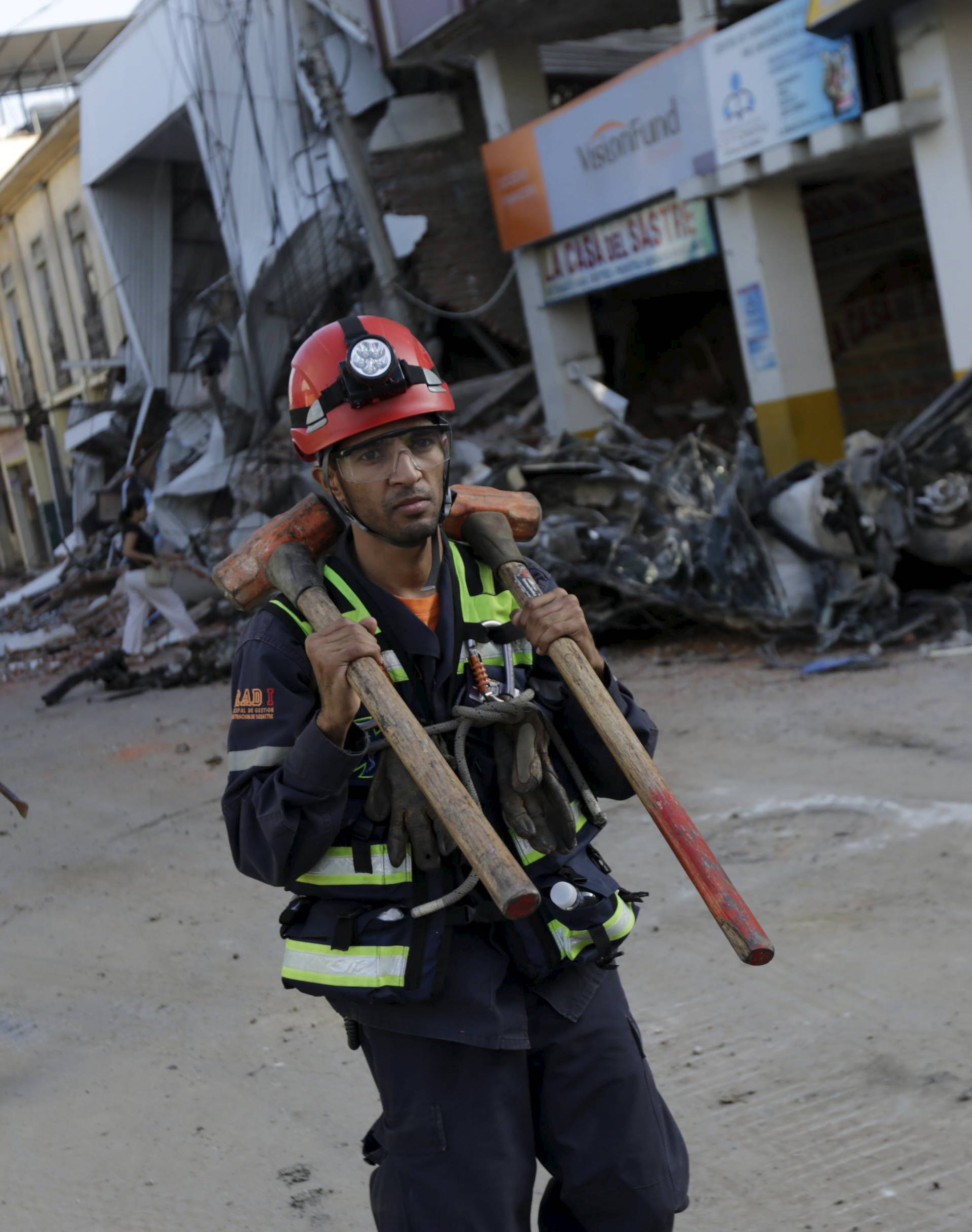 Rescue team members walk along a street past damaged building and debris after an earthquake struck off the Pacific coast, in Portoviejo