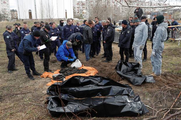 French forensics investigators watch as Ukrainian colleagues explore remains of bodies of burned civilians exhumed from a grave in the town of Bucha
