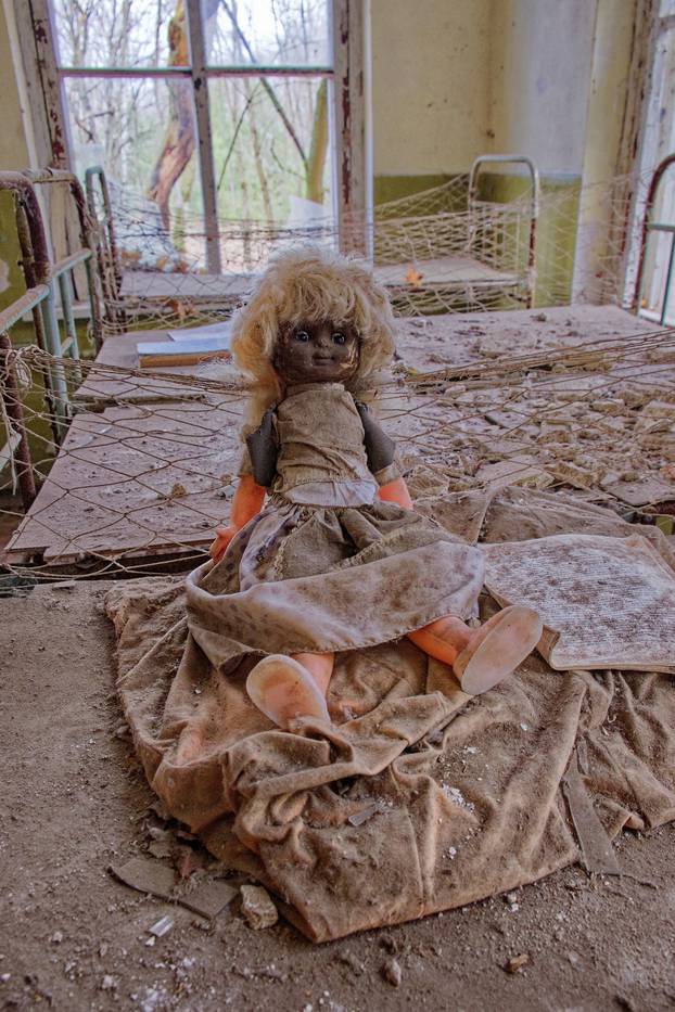 An abandoned room houses a doll with a sad expression. An old doll with a dirty face on a bed in an abandoned kindergarten. Radiation-contaminated room in Chernobyl.