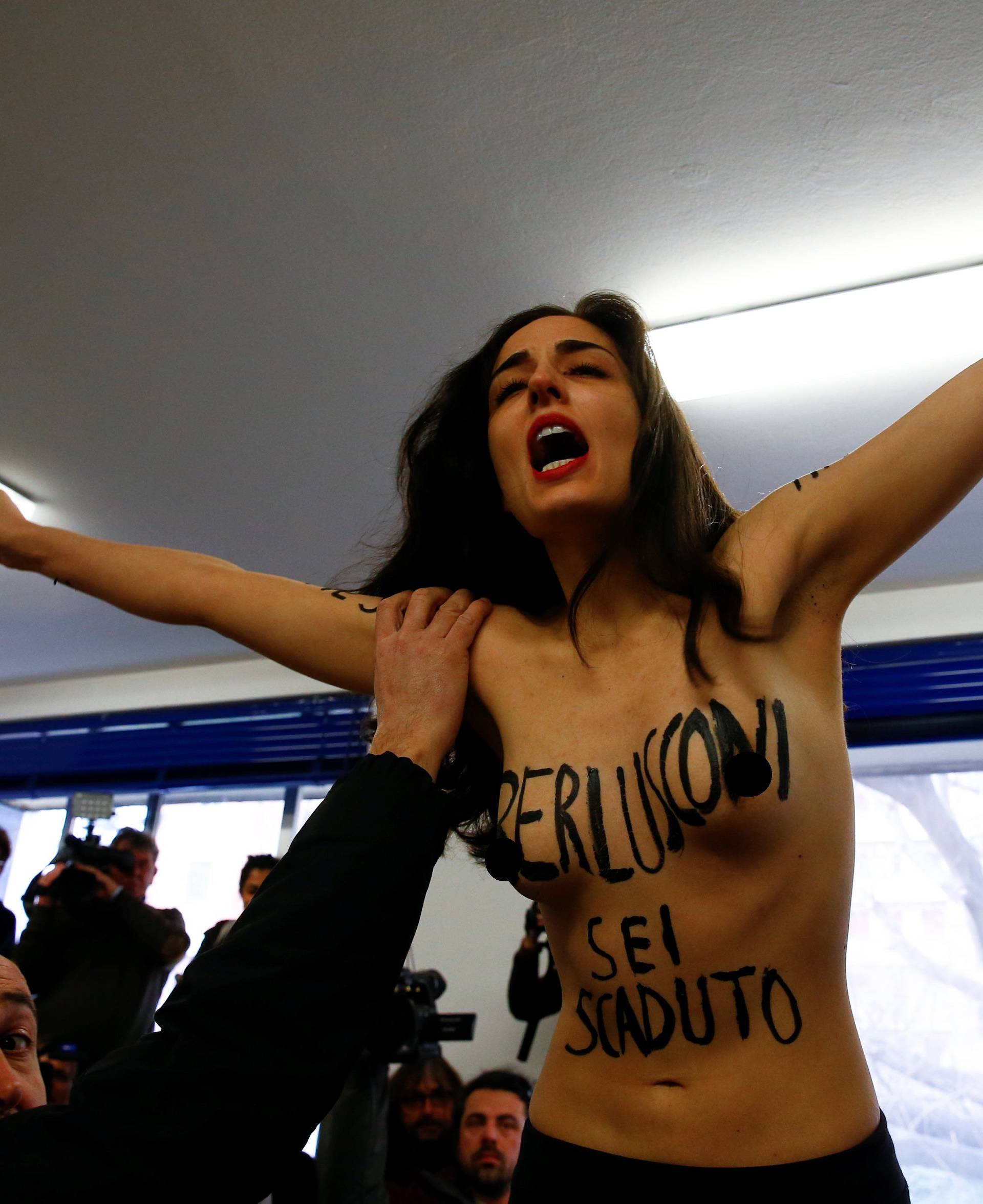 A topless activist of women's rights group Femen interrupts voting as Forza Italia party leader Silvio Berlusconi casts his vote at a polling station in Milan