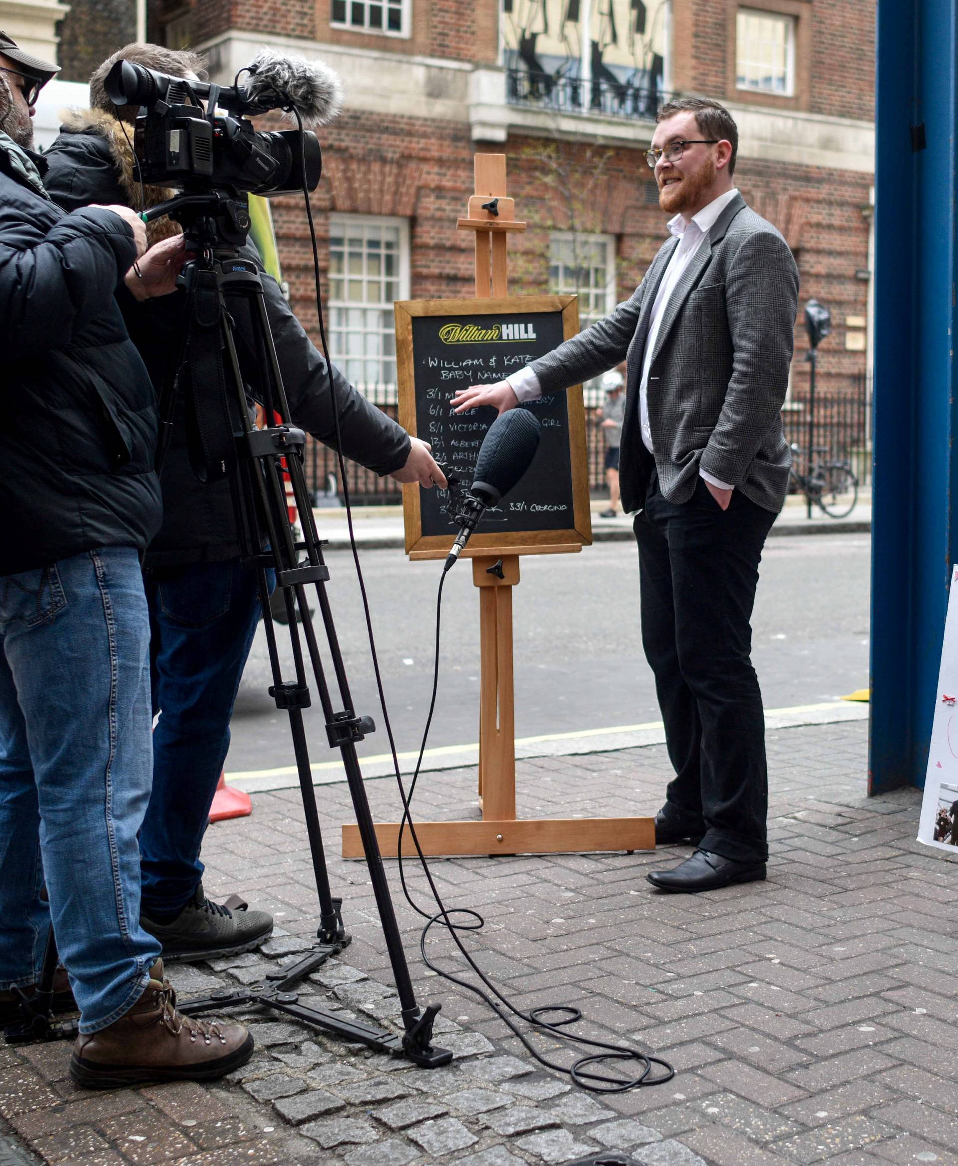A spokesperson from the bookmaker William Hill, is interviewed by a televsion crew as he writes the names and betting odds for the third royal baby of Britain's Prince William and Catherine, Duchess of Cambridge, on a board outside St Mary's Hospital