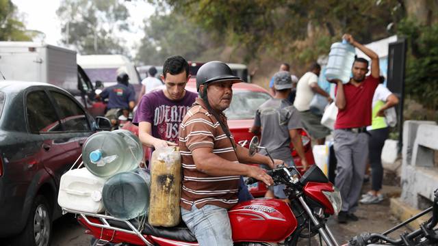 People carry bottles filled with water from a river in Caracas