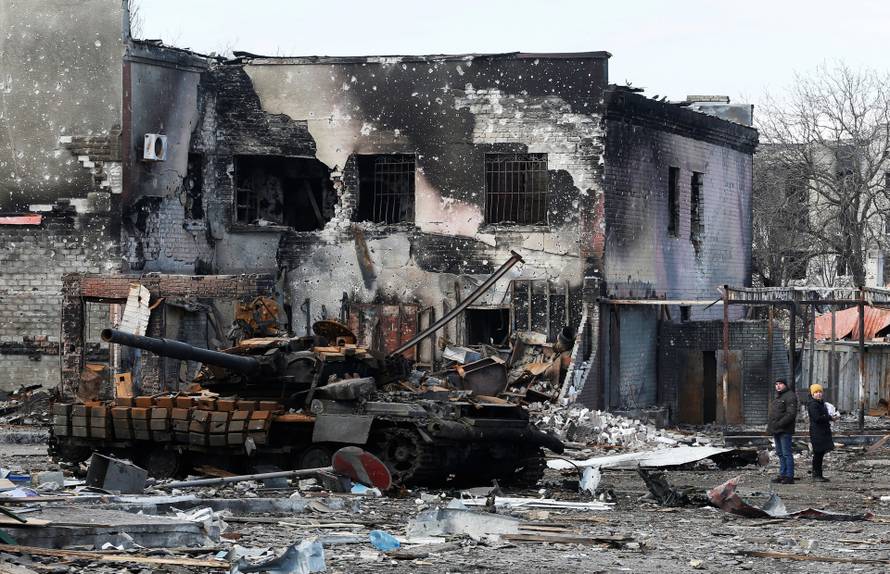 Local residents are seen next to a destroyed armoured vehicle in Volnovakha