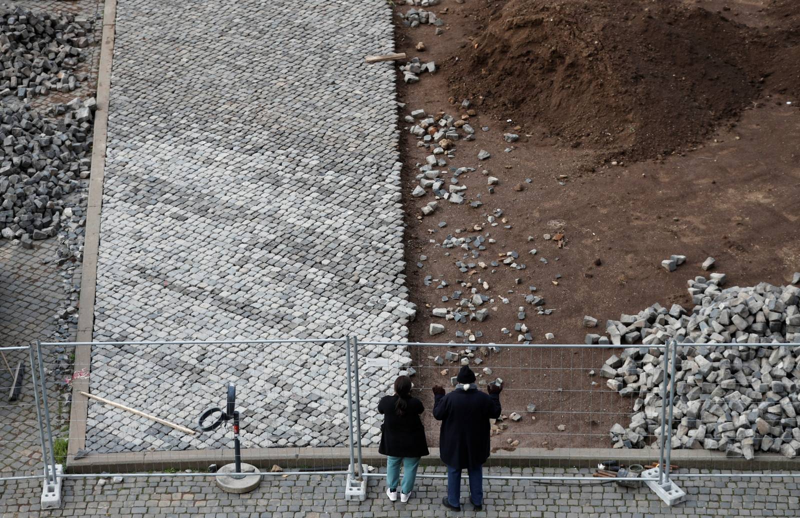 People look through a fence by the Colosseum, where work is being carried out to replace traditional cobblestones, in Rome