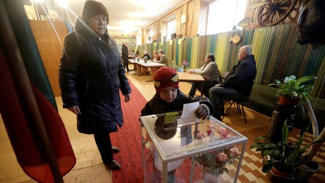A woman looks on as a child casts her vote during a general election run-off in Birzai