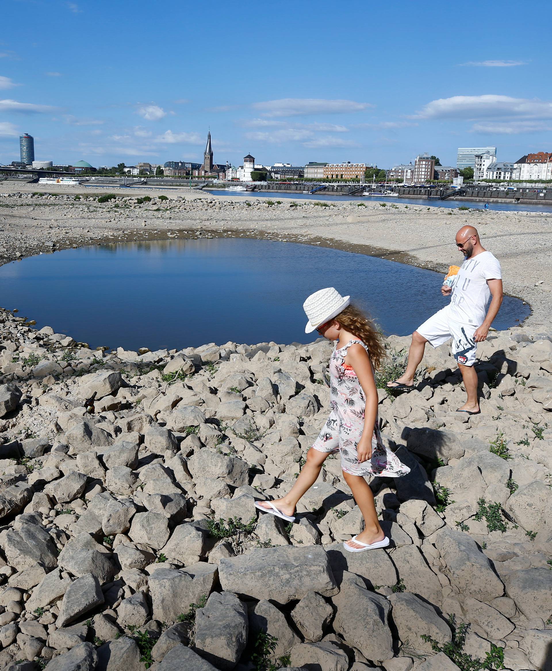 A family walks next to a puddle in the partially dried riverbed of Rhine, in front of the skyline of Dusseldorf