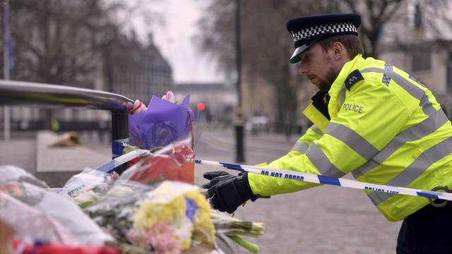 A police officer reaches out to floral tributes in Westminster the day after an attack, in London