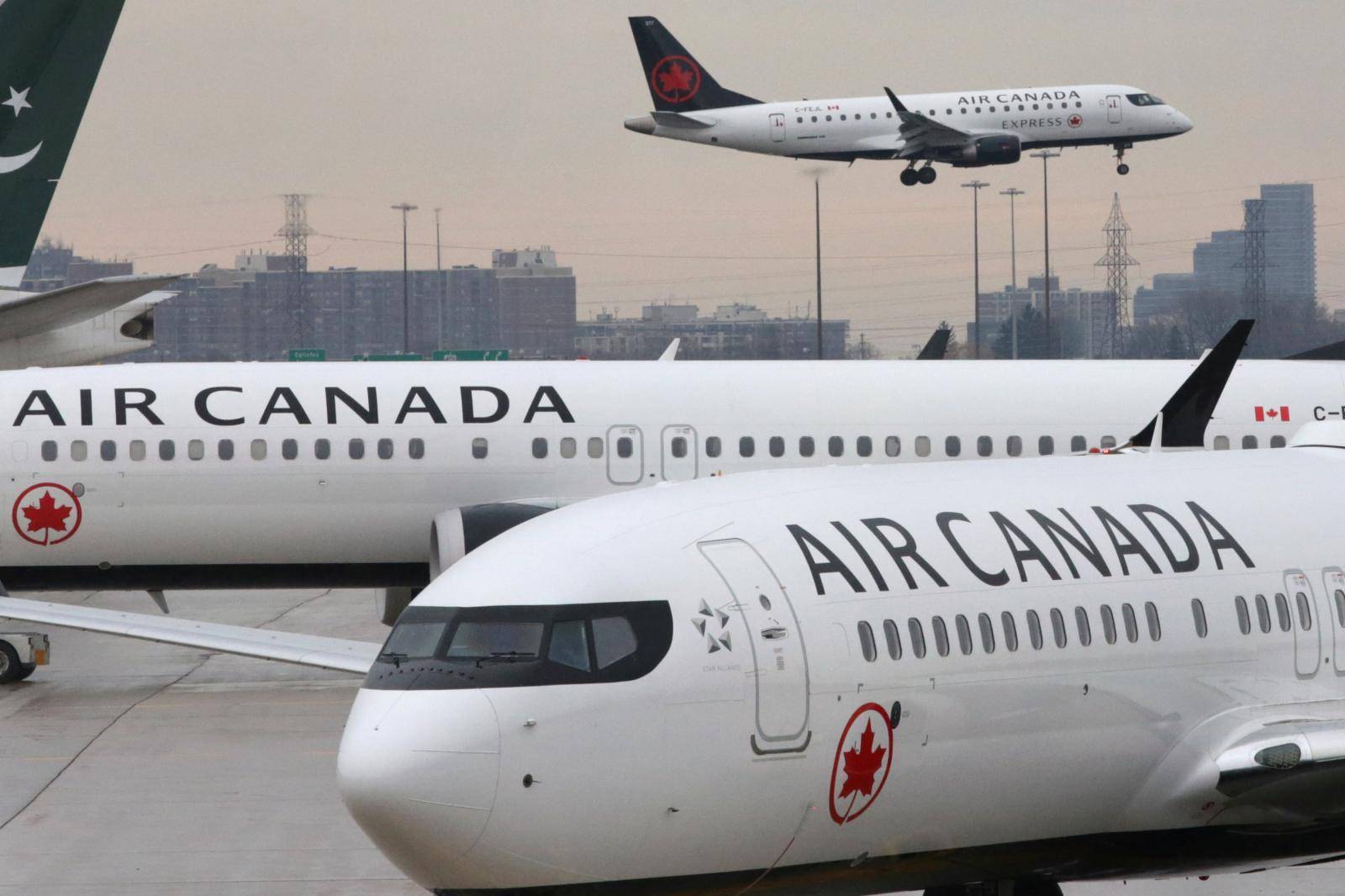 Two Air Canada Boeing 737 MAX 8 aircrafts are seen on the ground as Air Canada Embraer aircraft flies in the background at Toronto Pearson International Airport