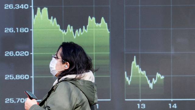 FILE PHOTO: A passerby wearing a protective face mask walks past an electric screen displaying a graph showing Japan's Nikkei share average, in Tokyo