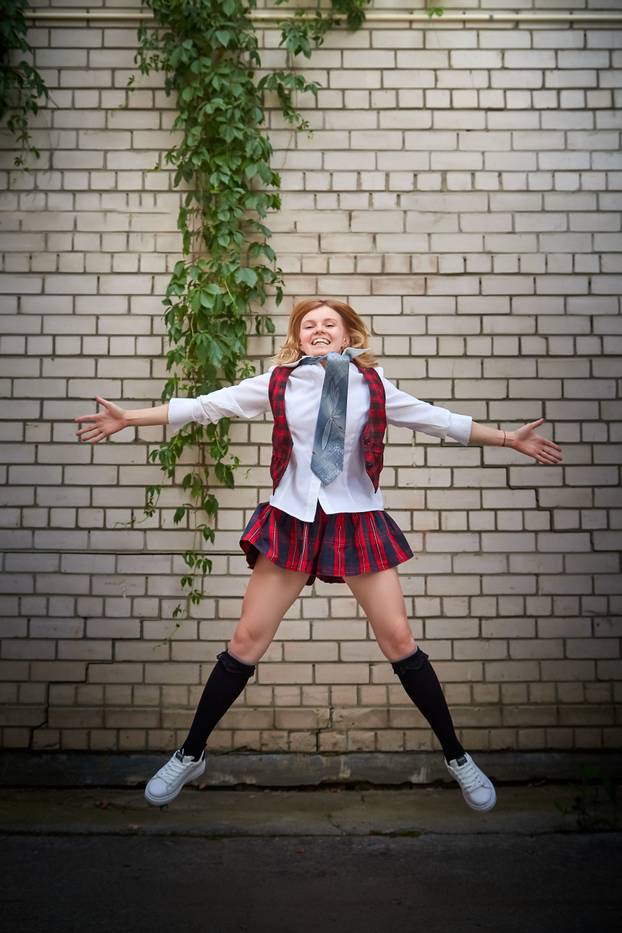 Young girl with short hair in a school checkered uniform outdoors.
