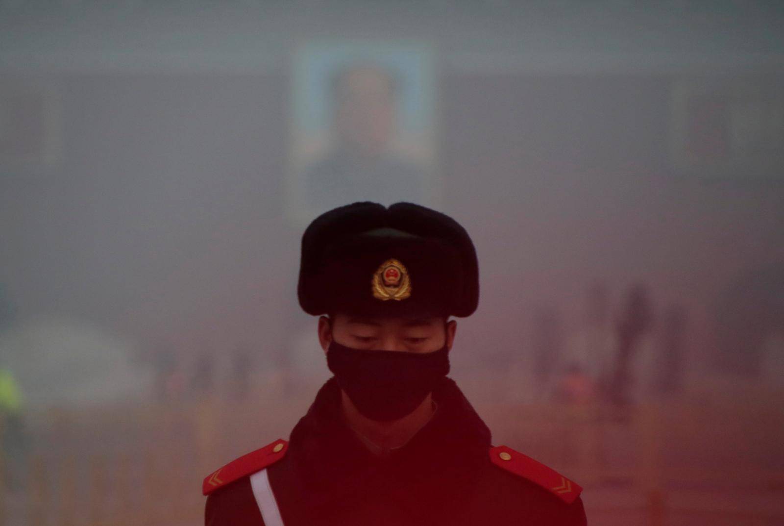 FILE PHOTO: A paramilitary police officer wearing a mask stands guard in front of a portrait of the late Chairman Mao during smog at Tiananmen Square in Beijing