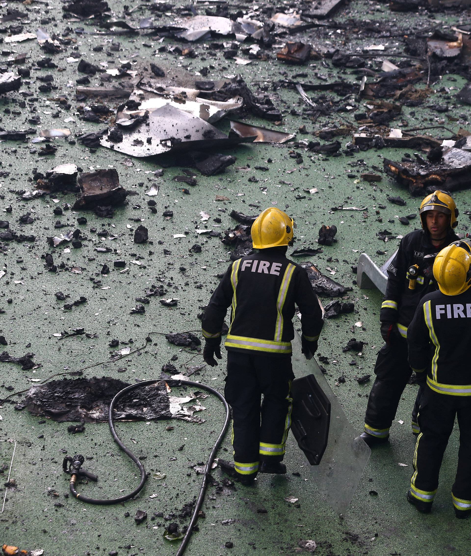 Firefighters stand amid debris in a childrens playground near a tower block severly damaged by a serious fire, in north Kensington, West London