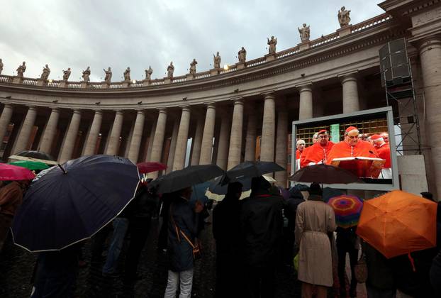 FILE PHOTO: People in Saint Peter's Square shelter from rain as they watch a live television screen showing cardinals entering the Sistine Chapel at the Vatican