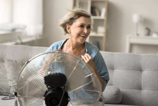 Cheerful carefree senior woman enjoying freshness from electric blower