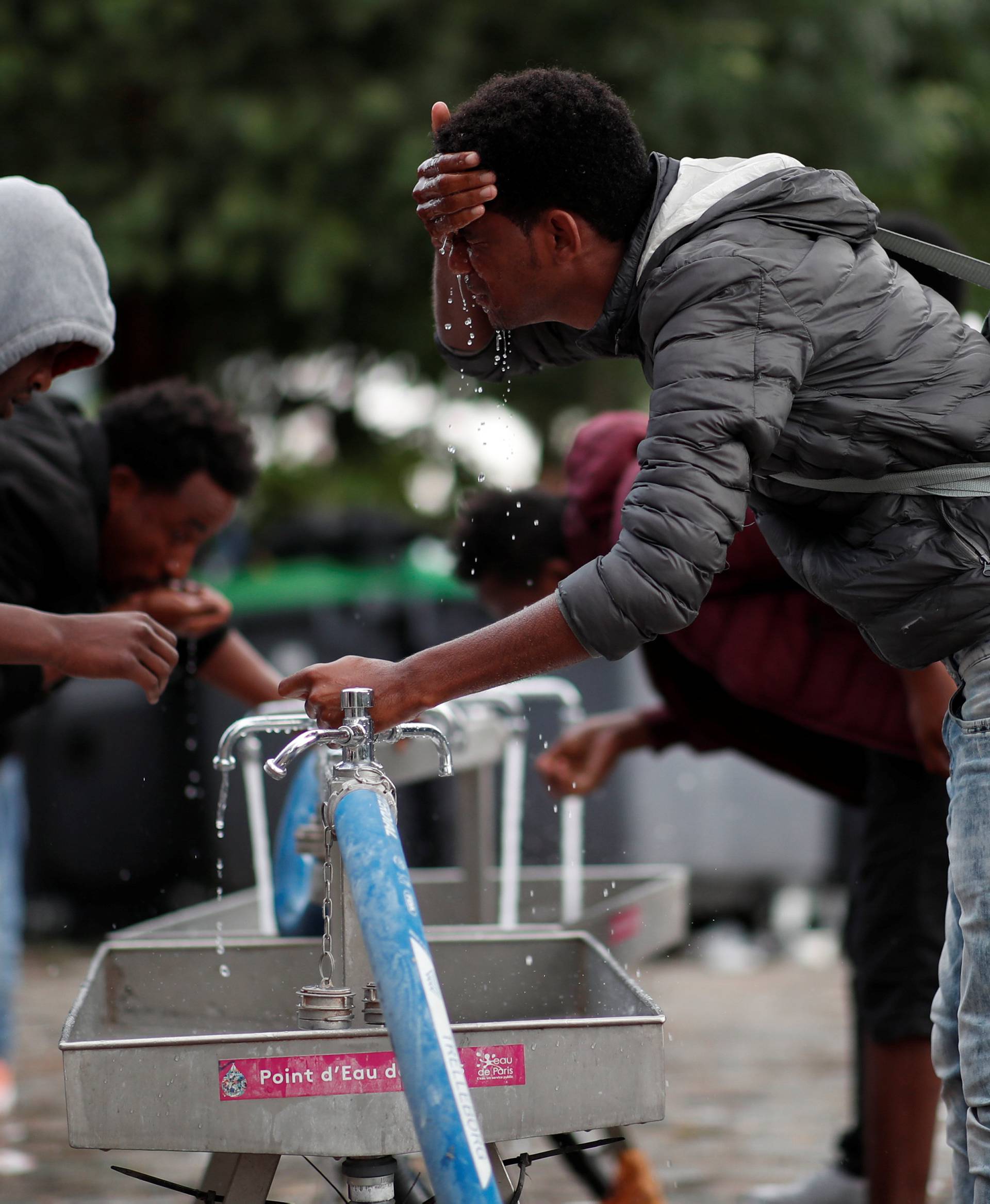 Migrants wash themselves as French police evacuate hundreds of migrants living in makeshift camps in Paris